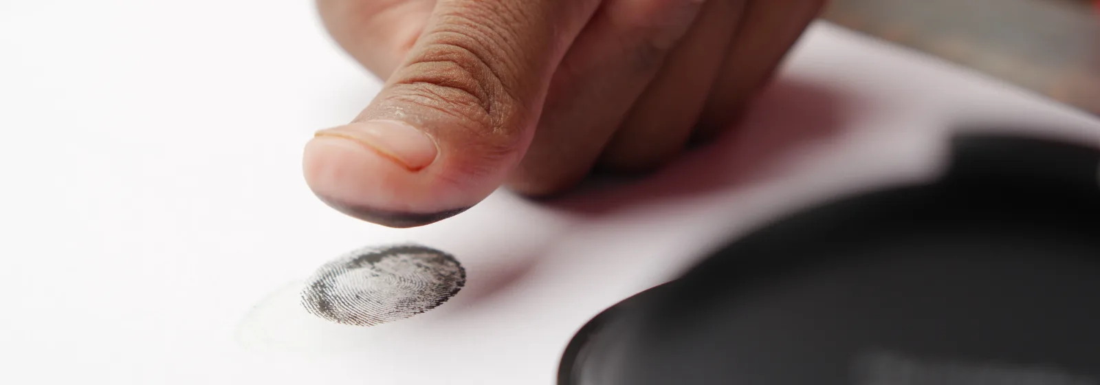 A thumb being pressed onto paper beside an ink pad to take a fingerprint